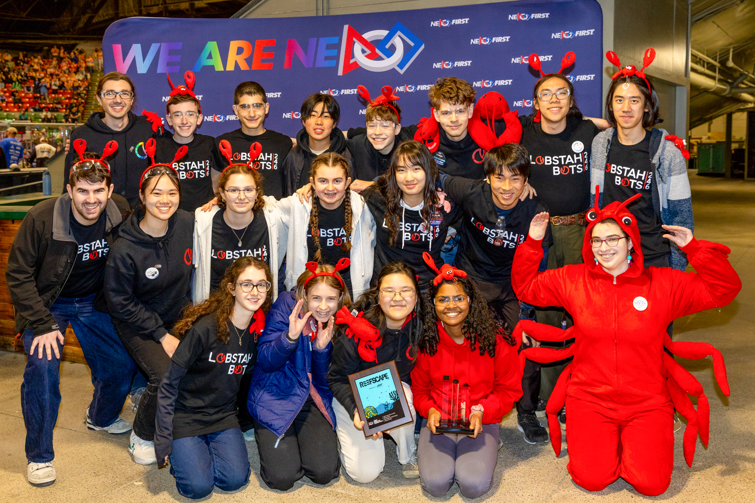 Students at a robotics contest holding an award, with one student dressed in a lobster costume
